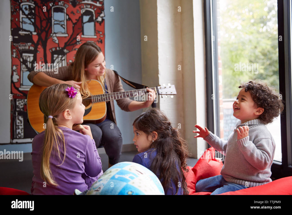 Teacher playing guitar while children enjoying at preschool Stock